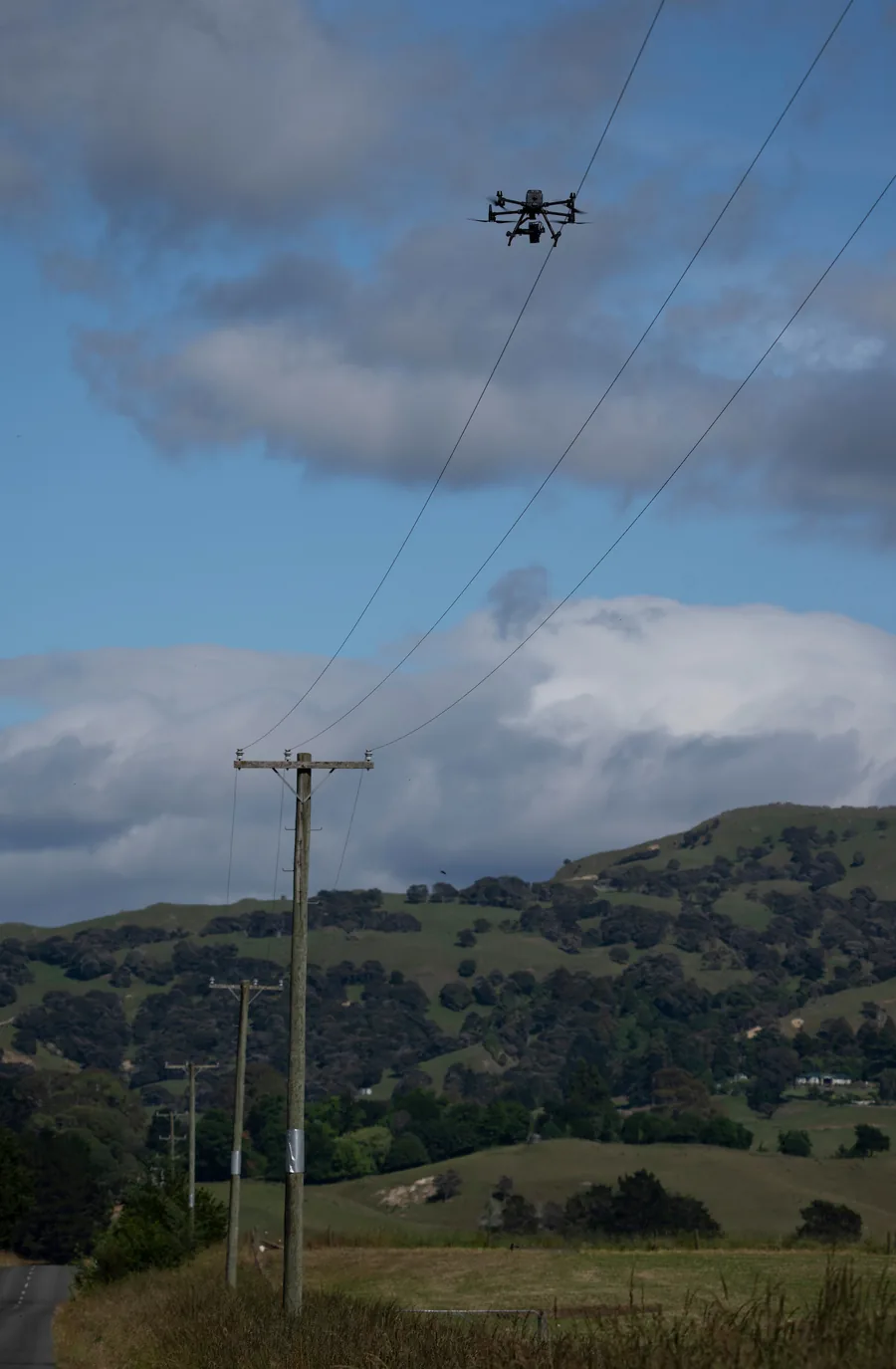 An inspection drone photographing a timber distribution pole above green hill country.