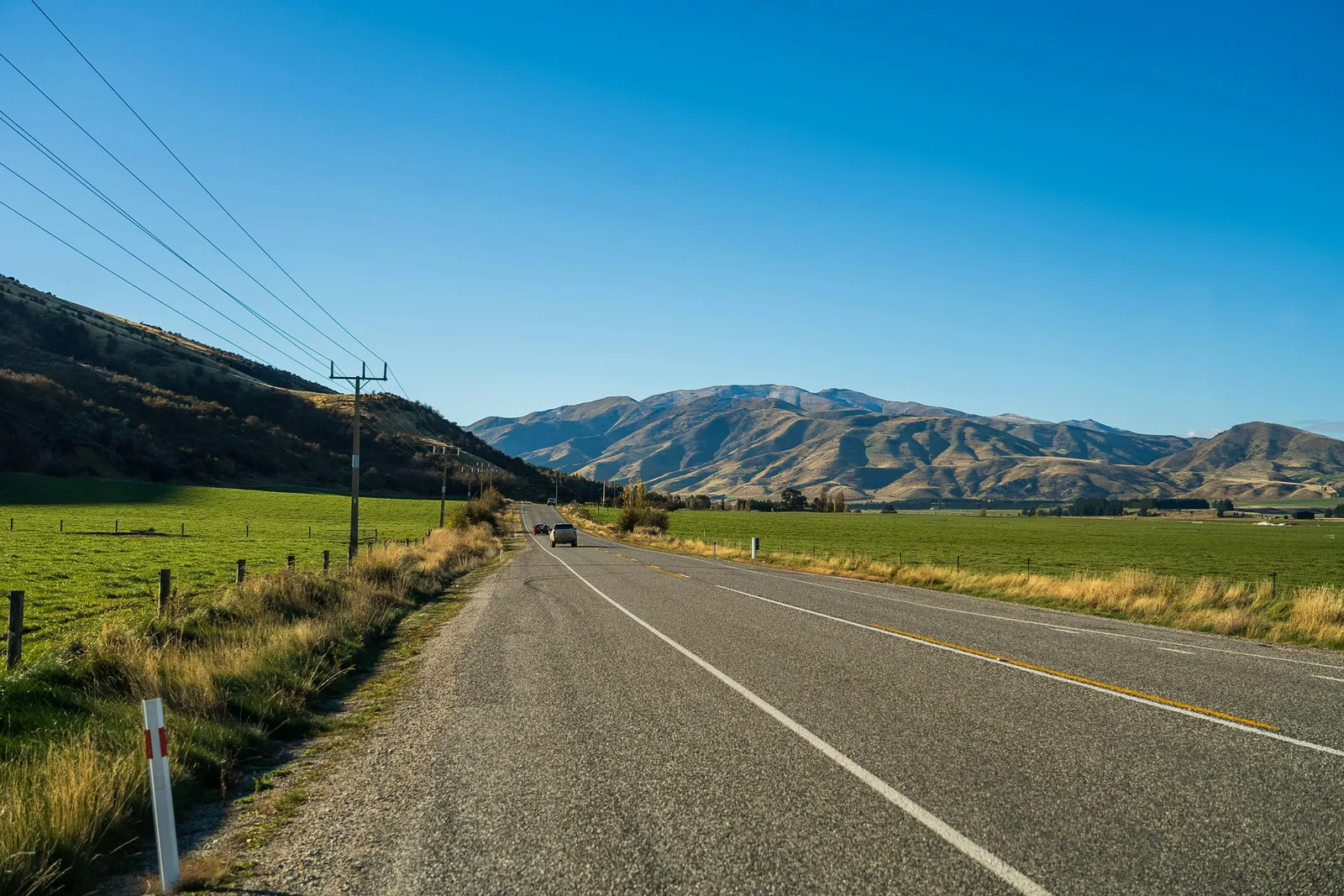 A rural highway with an overhead distribution line running alongside it through open farmland.