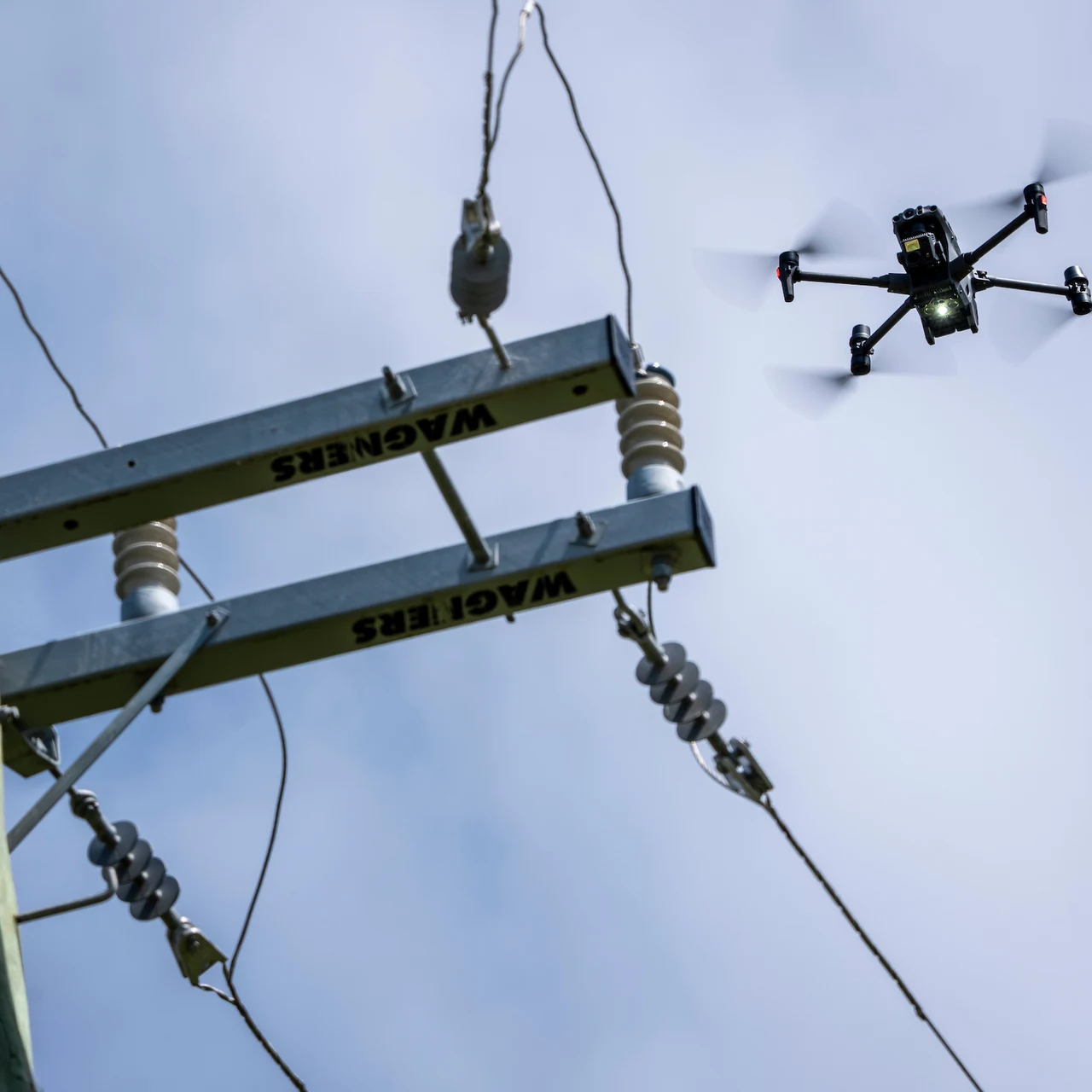 An inspection drone hovering beside a distribution pole crossarm, insulators and conductor terminations.