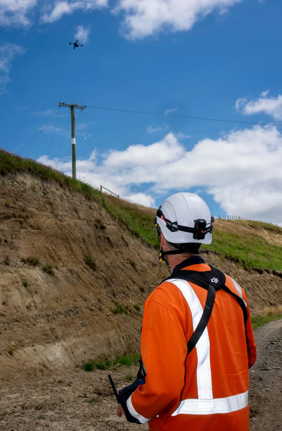 A field technician in high-visibility clothing flying an inspection drone over a line corridor.