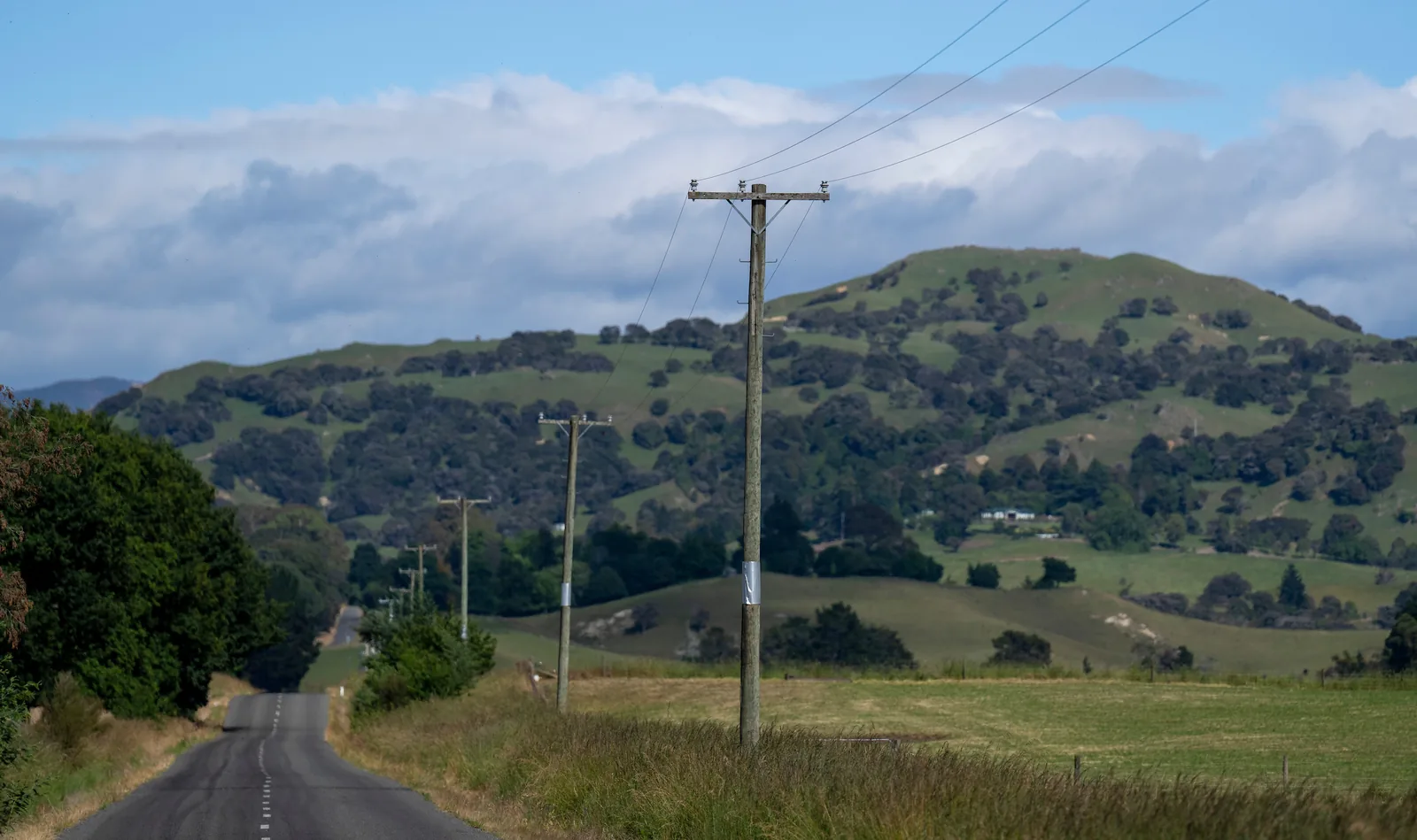 A rural road running beside a distribution line through green hill country.