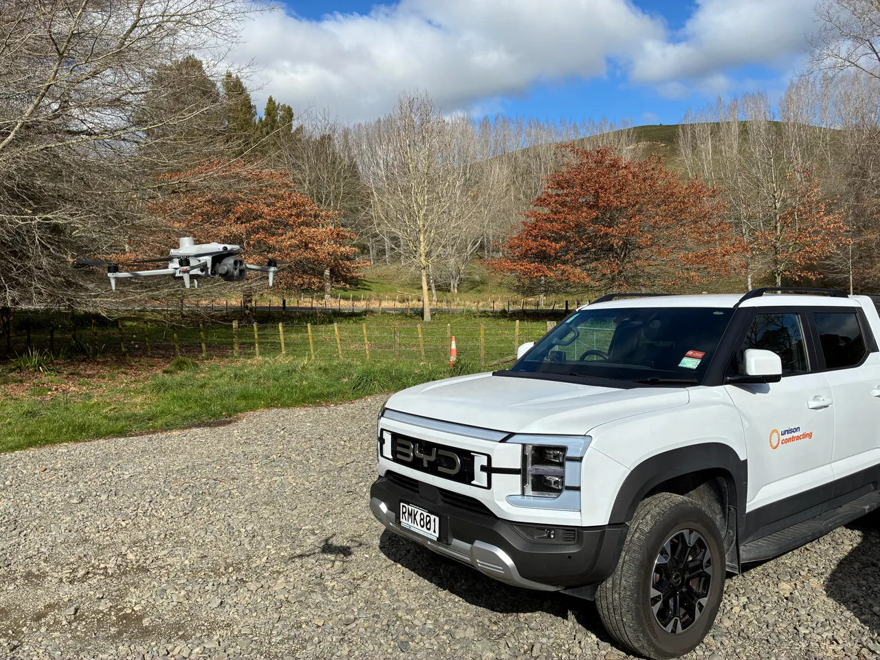 A field vehicle parked on a rural track while a drone is flown over the line.