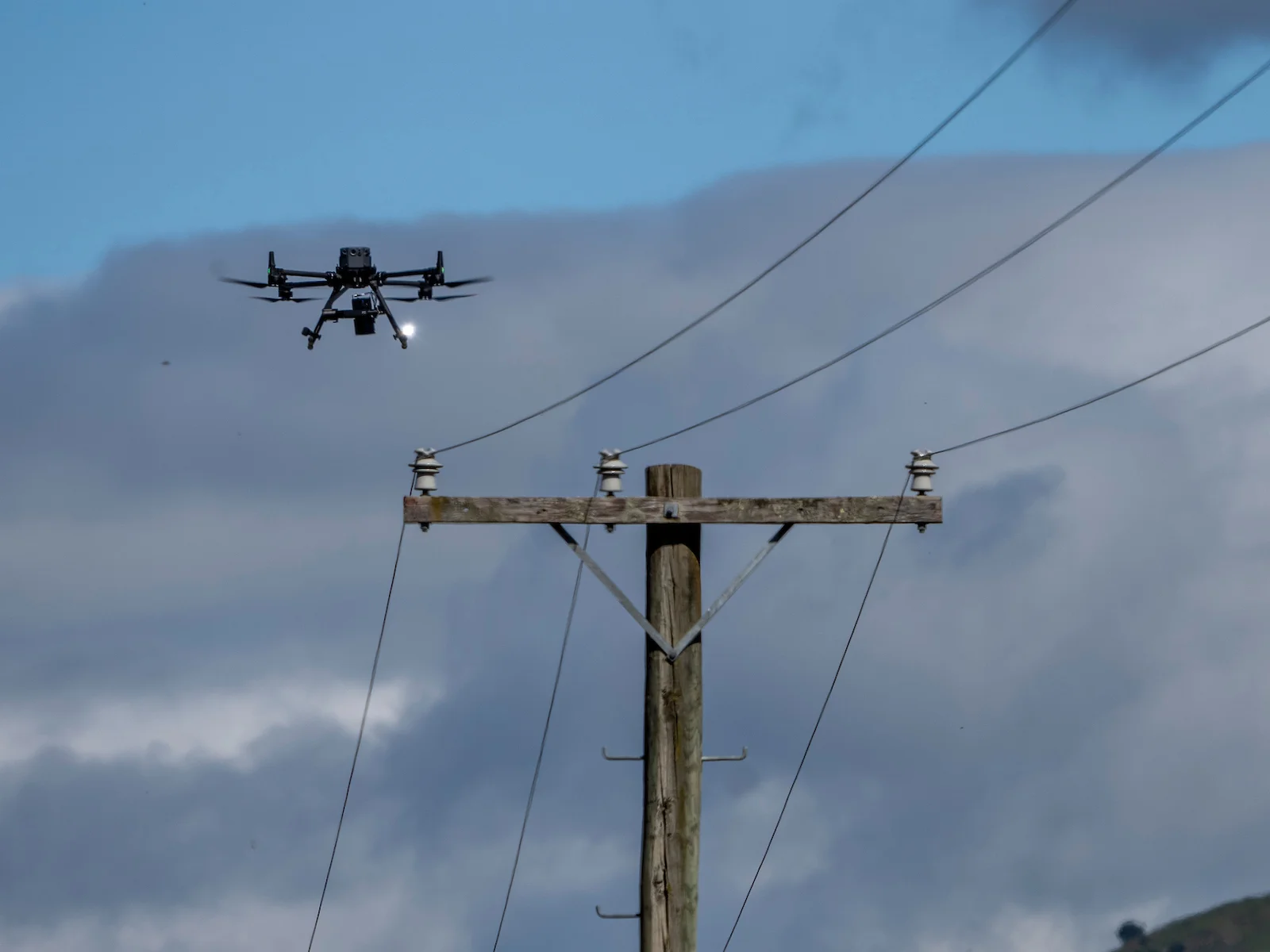 Close-up of a timber crossarm, insulators and conductors with an inspection drone alongside.