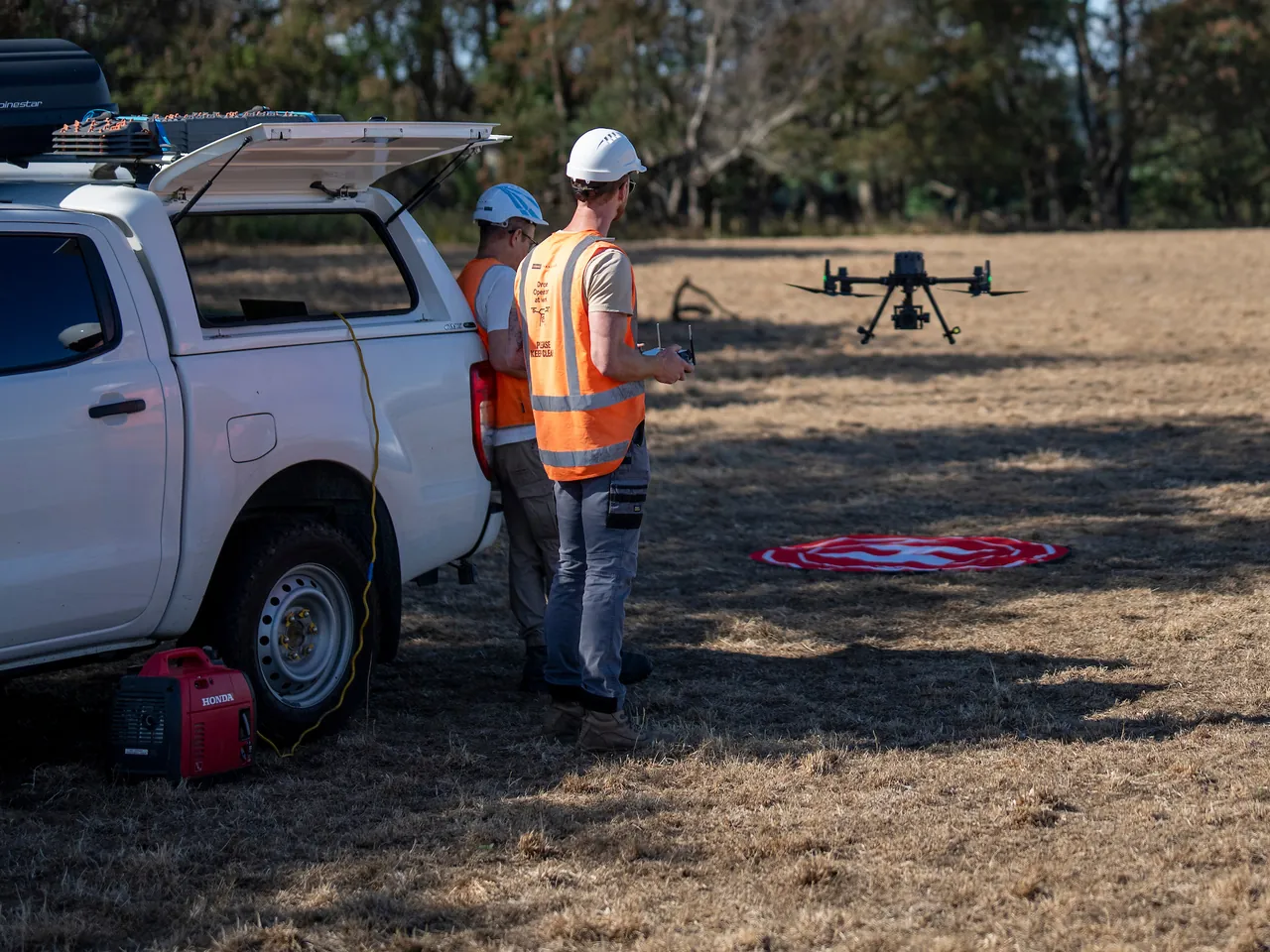 A field crew preparing an inspection drone beside a utility vehicle in a paddock.