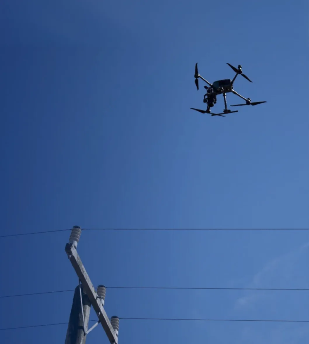 An inspection drone hovering beside the crossarm of a timber power pole.