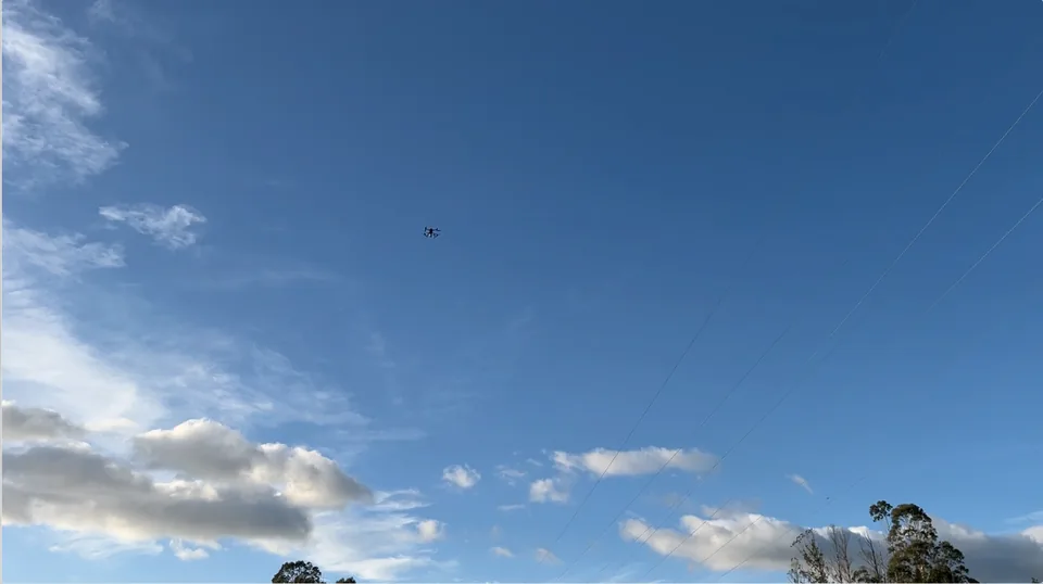 Open sky above a treeline with an inspection drone at altitude.