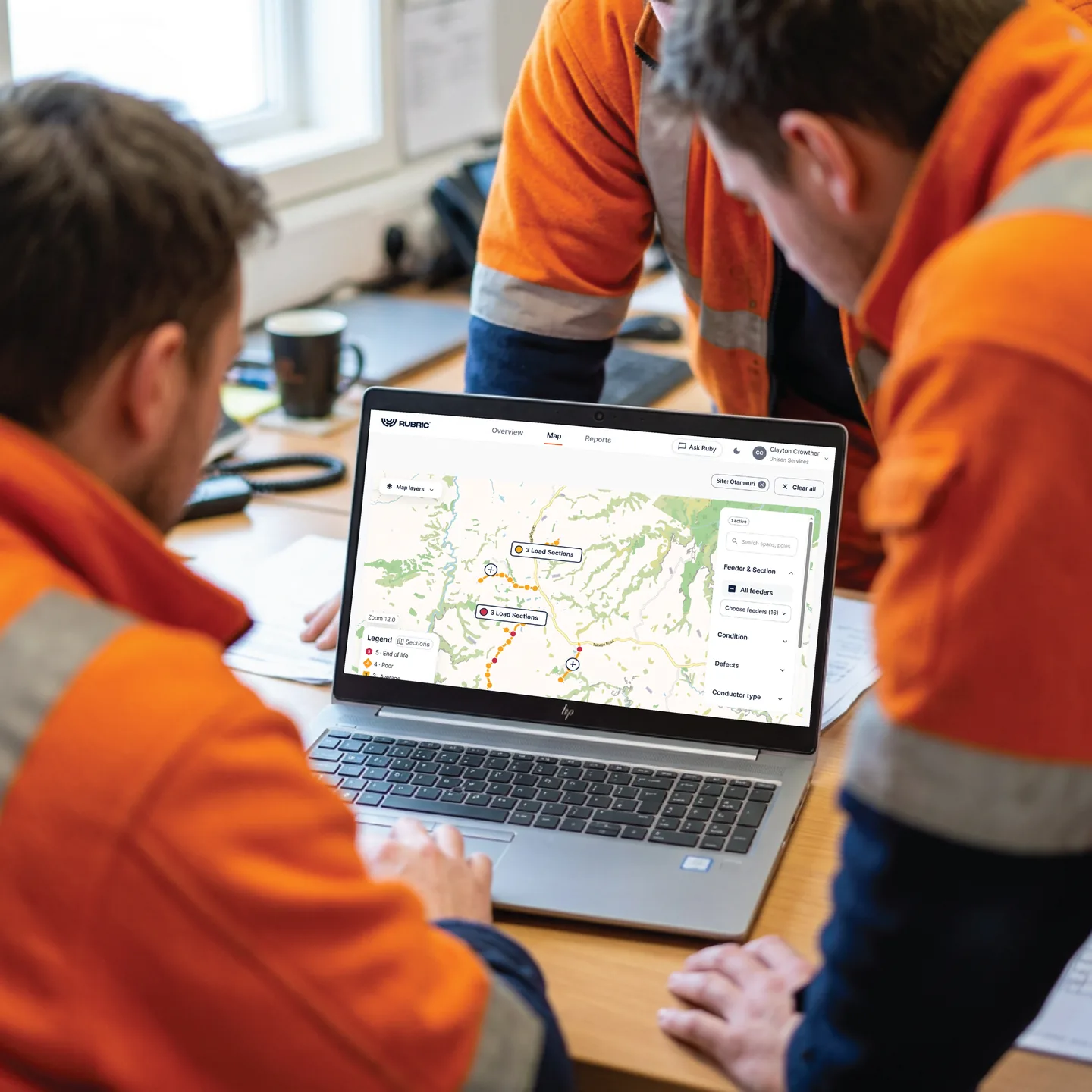 Two network staff in high-visibility clothing reviewing line condition data on a laptop.